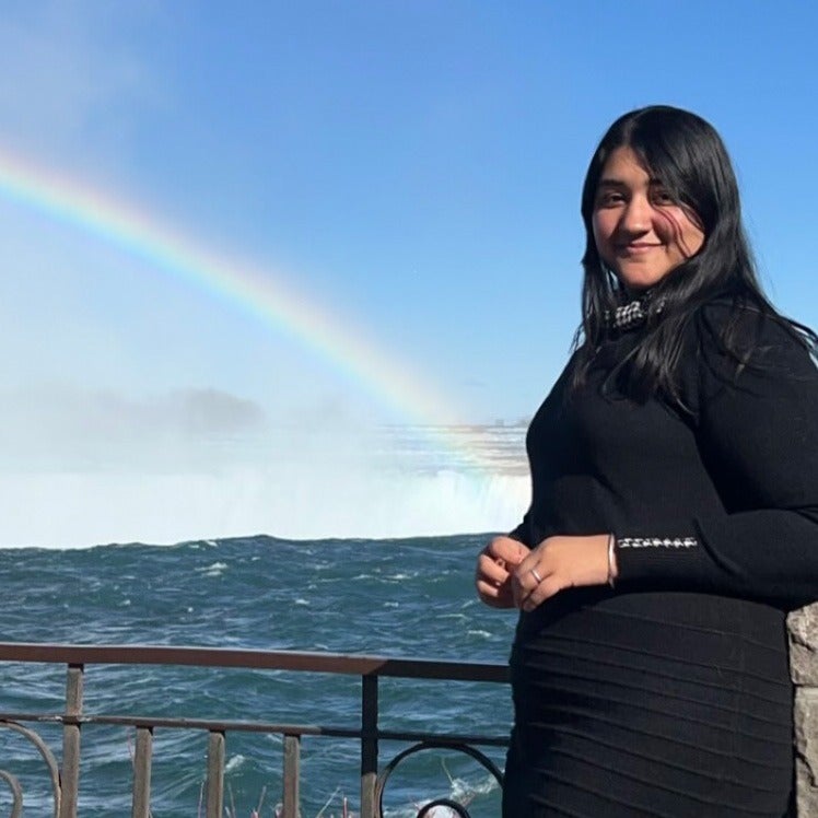 Pallavi standing in front of waterfalls with a rainbow