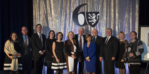 Group of people standing in front of a silver curtain with 60th anniversary logo