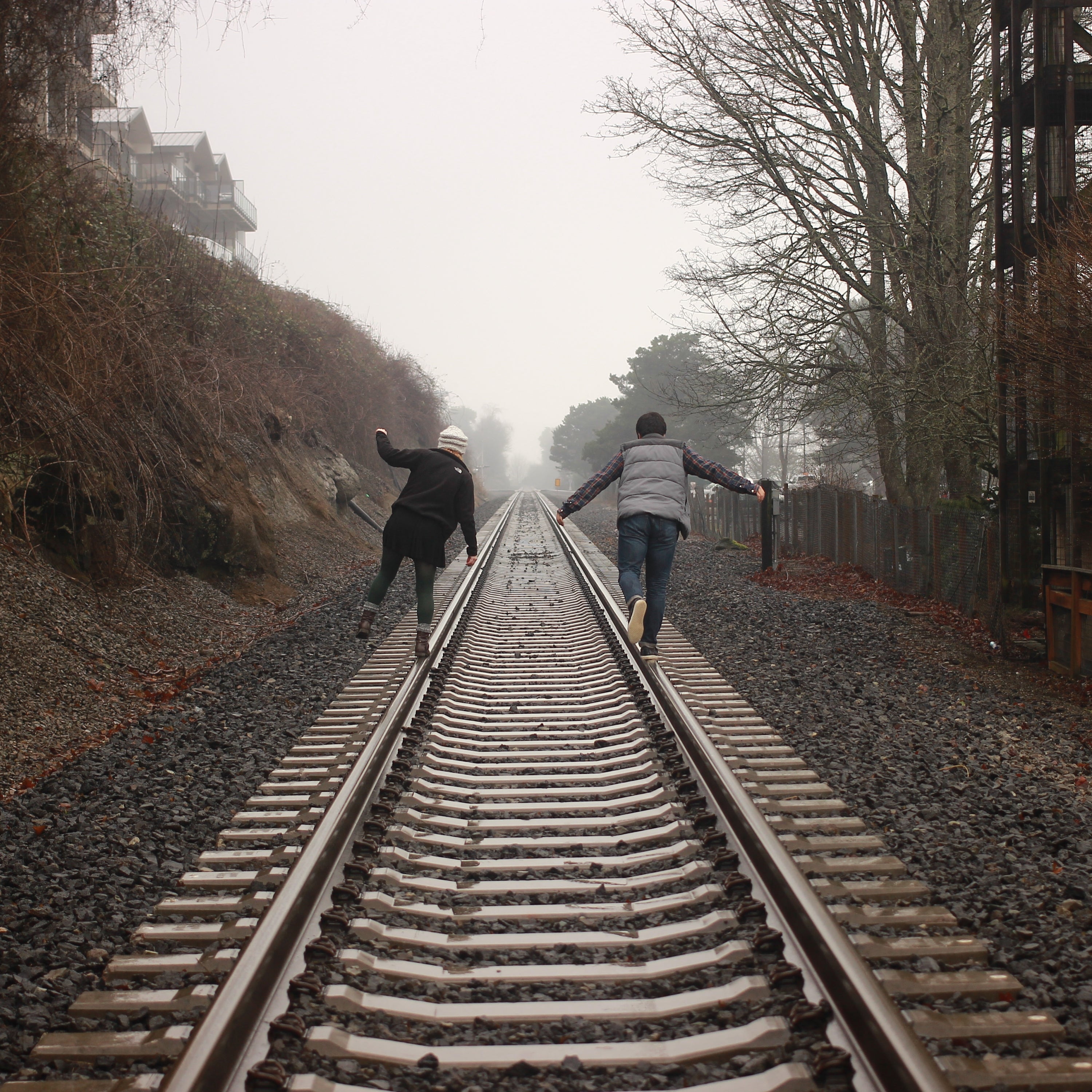 two people balancing on railroad track\
