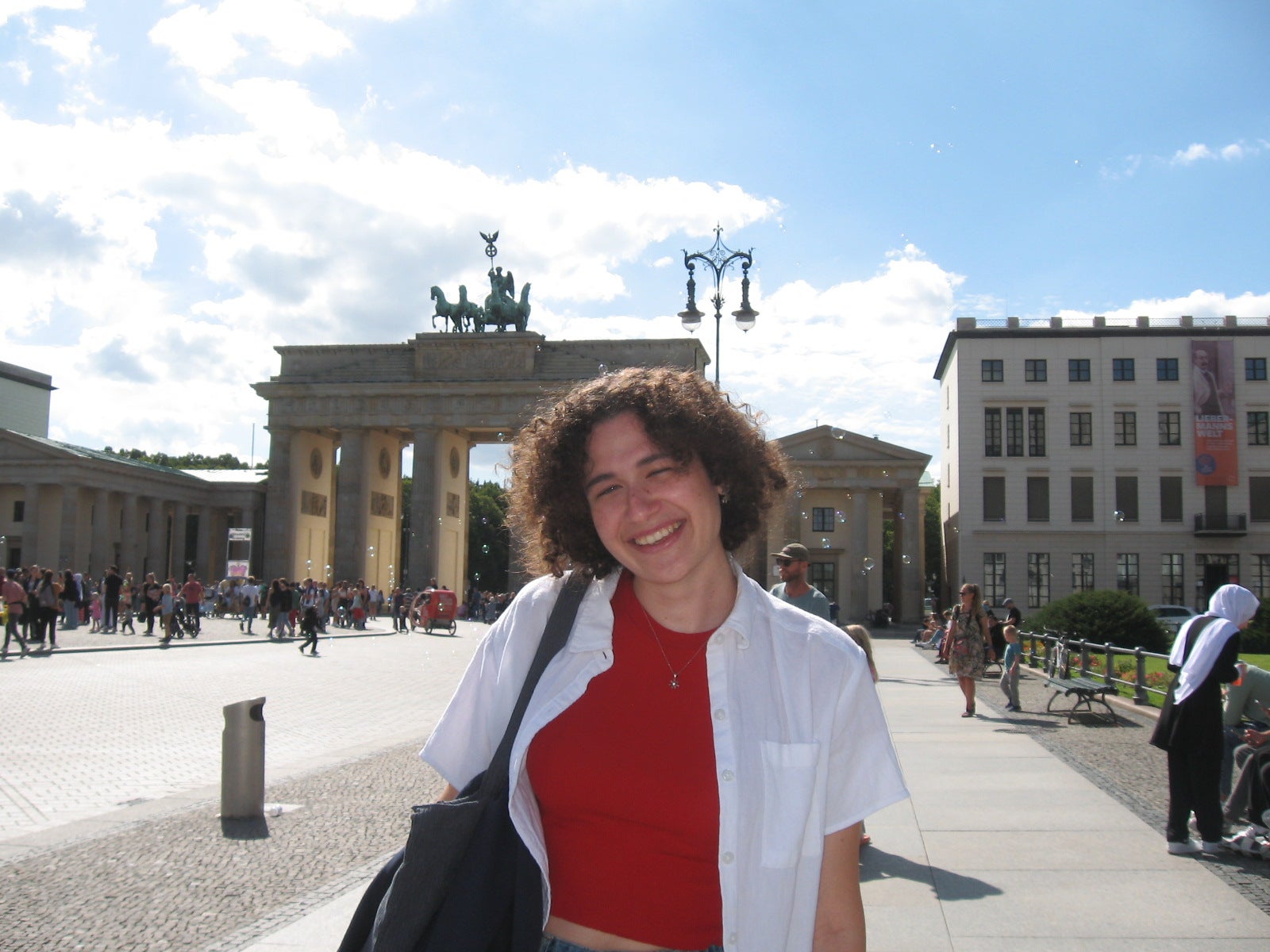 Person in a red shirt and white blouse standing in front of Brandenburg Gate, Germany. 