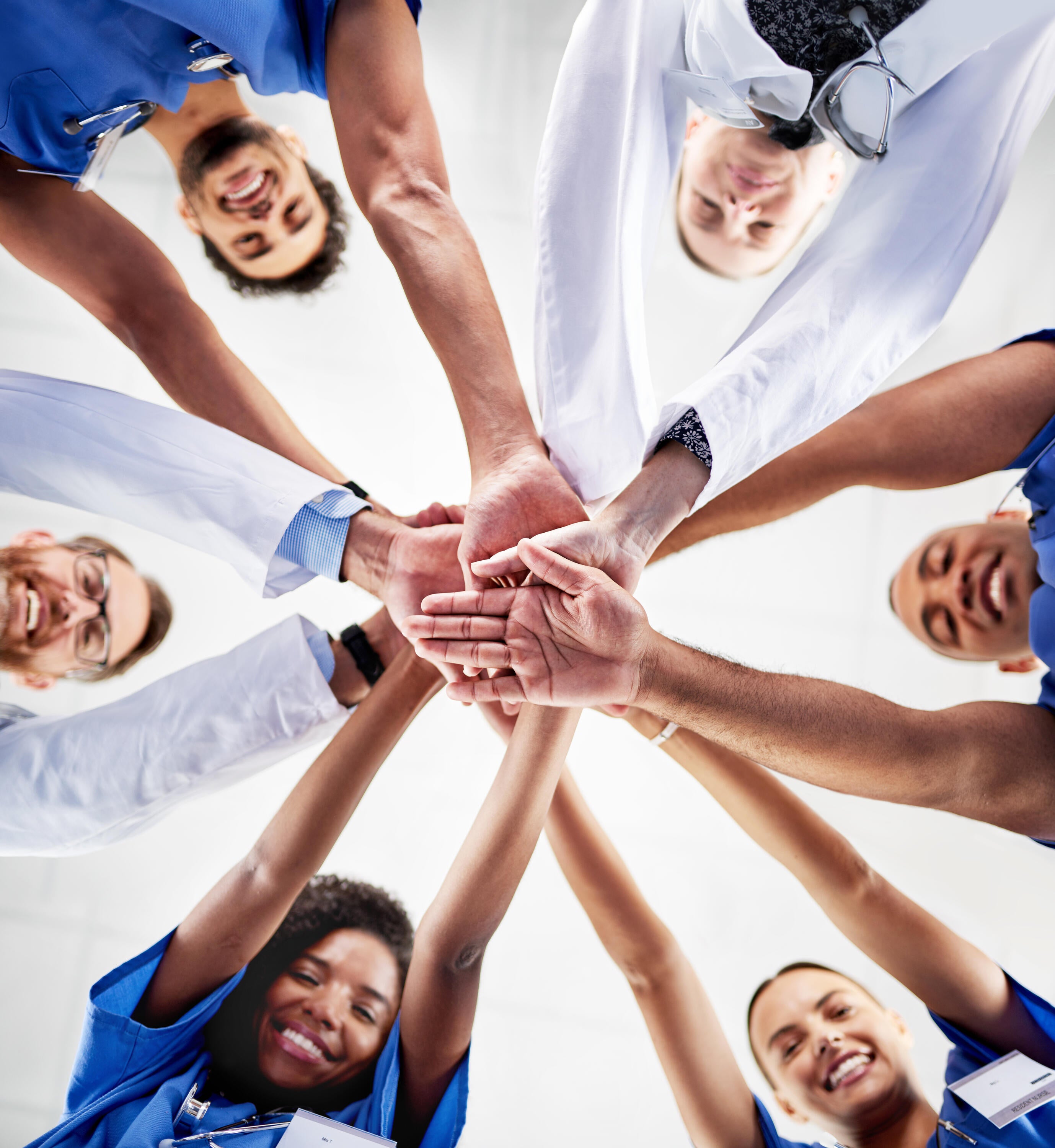 A team of healthcare professionals in a circle and their hands placed on top of each other in the middle of the circle, symbolizing teamwork and collaboration