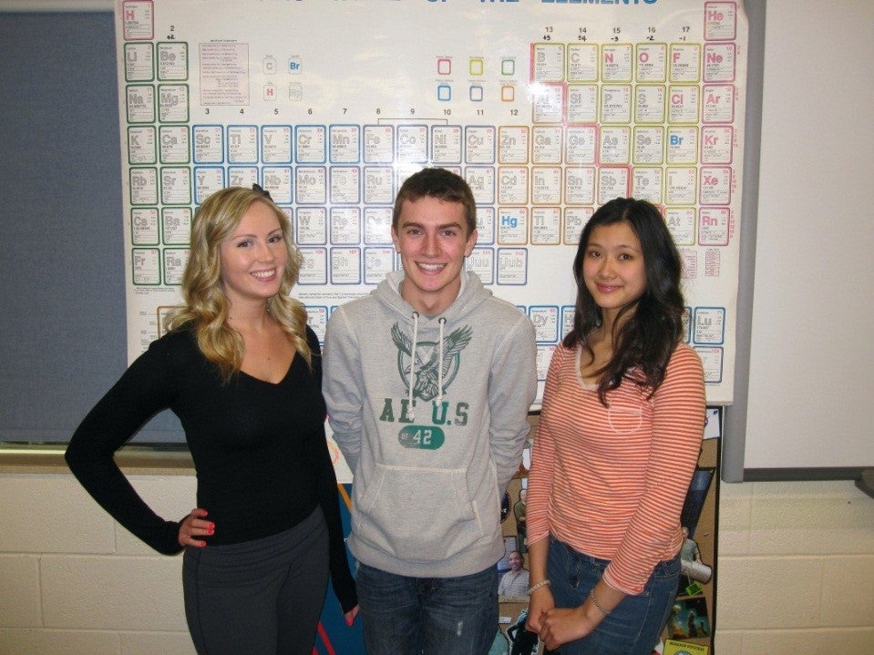 Three students standing in front of periodic table.