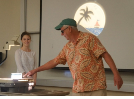 Two people use projector showing palm tree and boat drawing.
