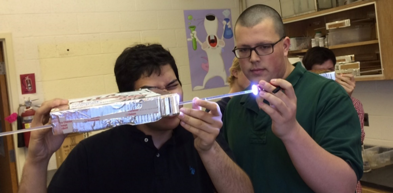 Two students with a lighted rod shining into a box.