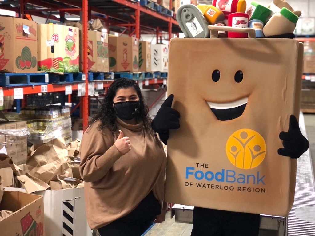 Vanessa standing with the Food Bank of Waterloo Region's mascot, both giving thumbs up.