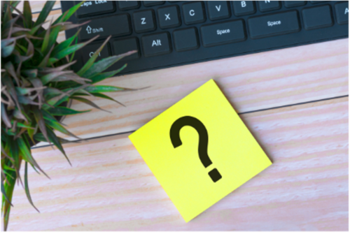 A post-it note with a question mark in front of a laptop keyboard.