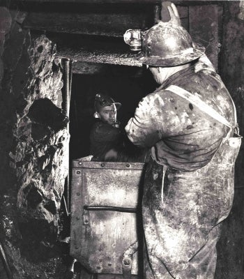 2 men wearing hard hats and other equipment work together in a mine tunnel underground