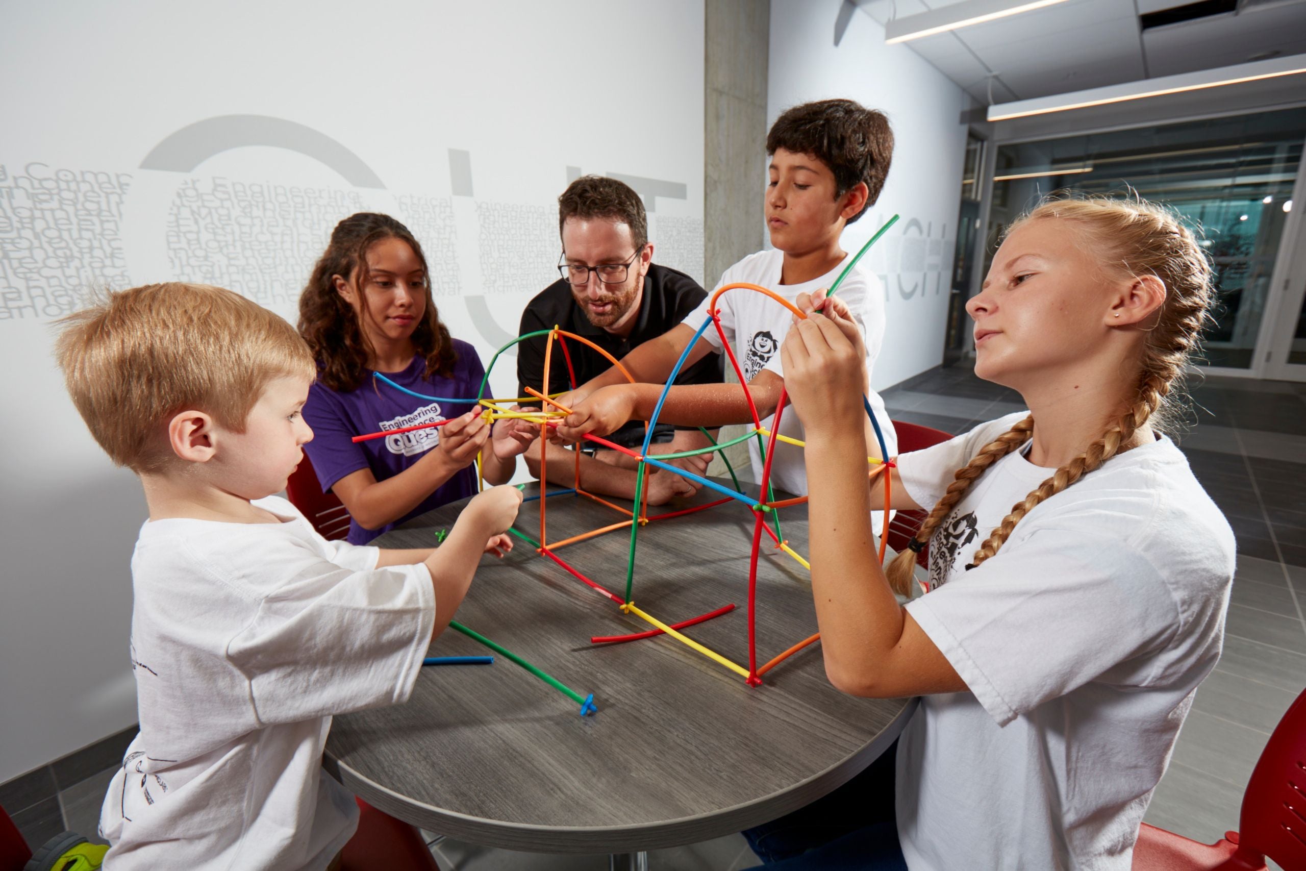 Three children and two volunteers building structures at a table