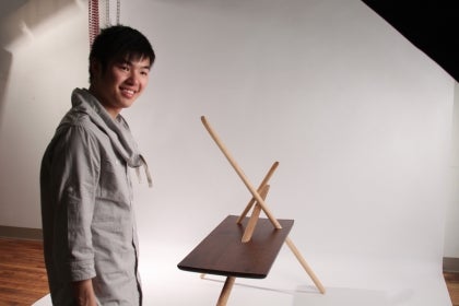 A student posing infront of his chair project in the photo studio." title="A student posing infront of his chair project in the photo studio.