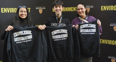 Students holding up Knowledge Integration hoodies