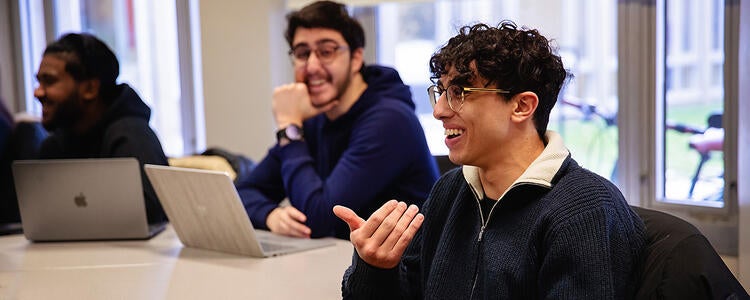 Students laugh while sitting at a table with a laptop