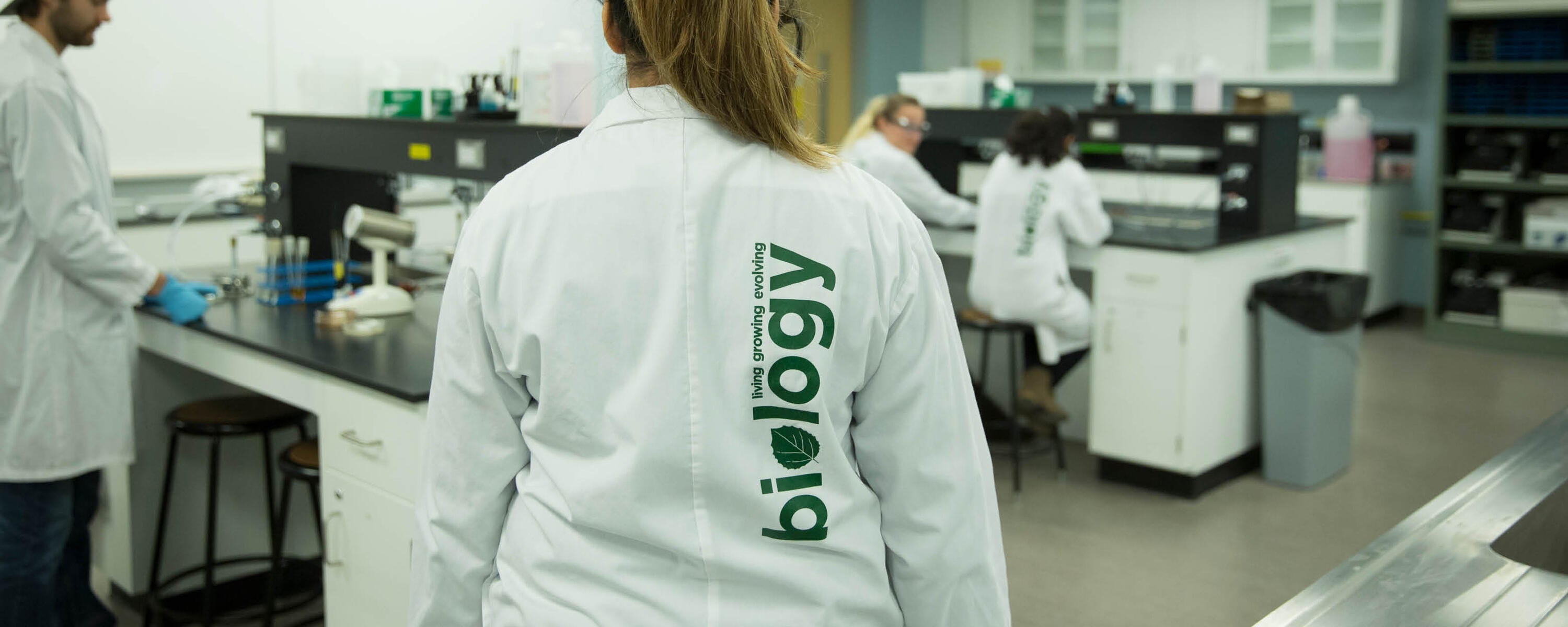 Student wearing lab coat with the words living, growing, evolving, biology on it.