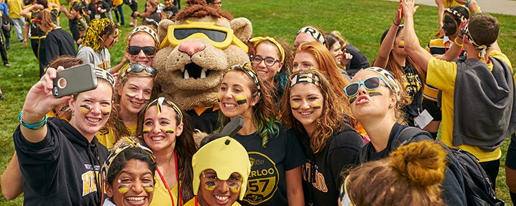 Students in Waterloo gear, taking a photo with mascot.