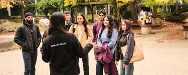 A student wearing a black jacket with ambassador on it faces a group of students