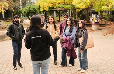 a student with ambassador on her jacket speaks with students facing her