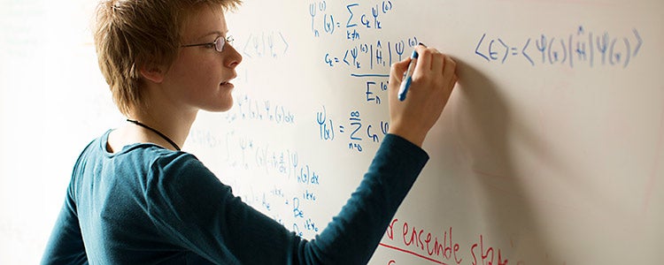 Female mathematical physics student writes formulas on white board.
