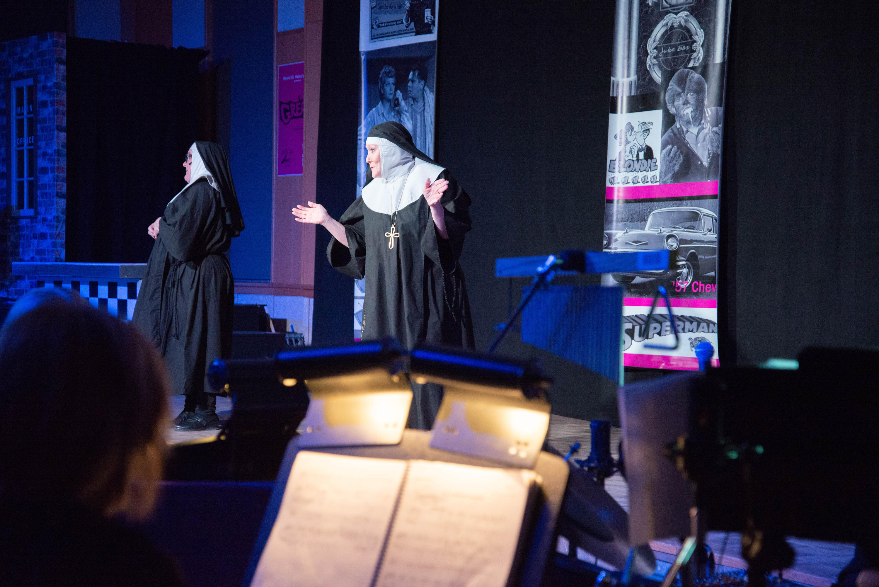 A nun sings on stage with a musician in the foreground