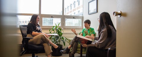 Two students sit in a bright office speaking to Gemma, the student life and recruitment coordinator. The grebel residence can be seen in the window to the outside behind them