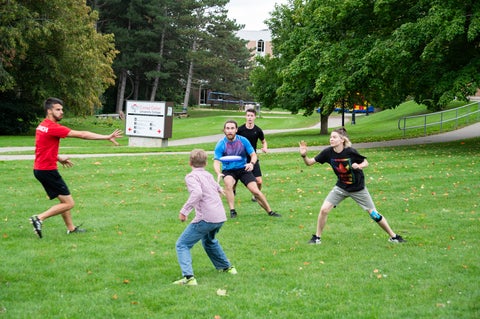 five grebel alumni play ultimate frisbee on the lawn outside United college