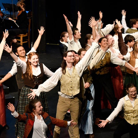 Students performing Something Rotten play on stage with arms in the air