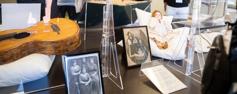 A close up of a display of physical objects from the mennonite archives of ontario. A doll, old pictures, and a guitar.