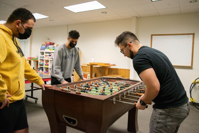 Two students playing foosball in Grebel games lounge, another student watches
