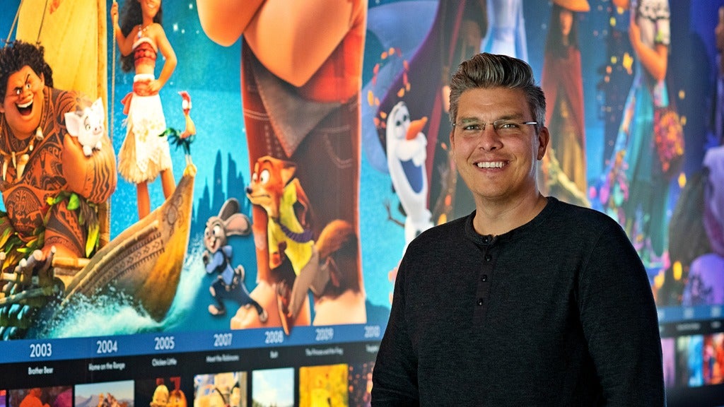 Greg Culp standing in front of a timeline of Disney movies he helped animate