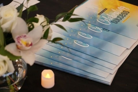 A table with flowers, a battery-powered candle and printed programs for the Recognition Reception event