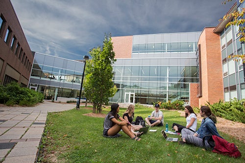 Five students sit on grass chatting in Faculty of Health courtyard.