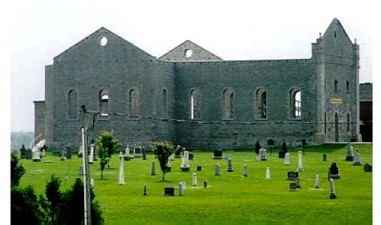 Neglected church ruins, walls intact, roofless, with graveyard in front