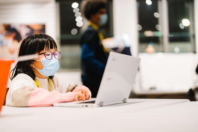 Little girl wearing a mask sitting at a desk on a laptop at LAUNCH Waterloo