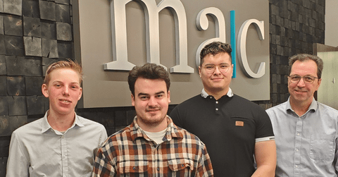 MAC LLP co-op students and employee standing in front of logo at the office