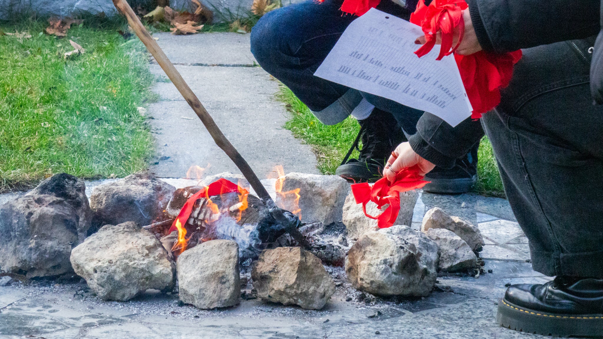 Participant carefully placing red fabric ties into s fire along with a list of names