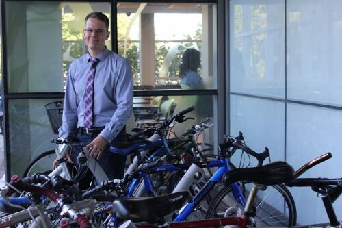 Professor Markus Moos standing beside a bicycle parked in a bike rack