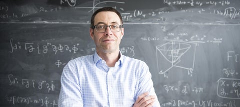 Dr. Will Percival standing in front of a chalkboard with scientific formulas written on it