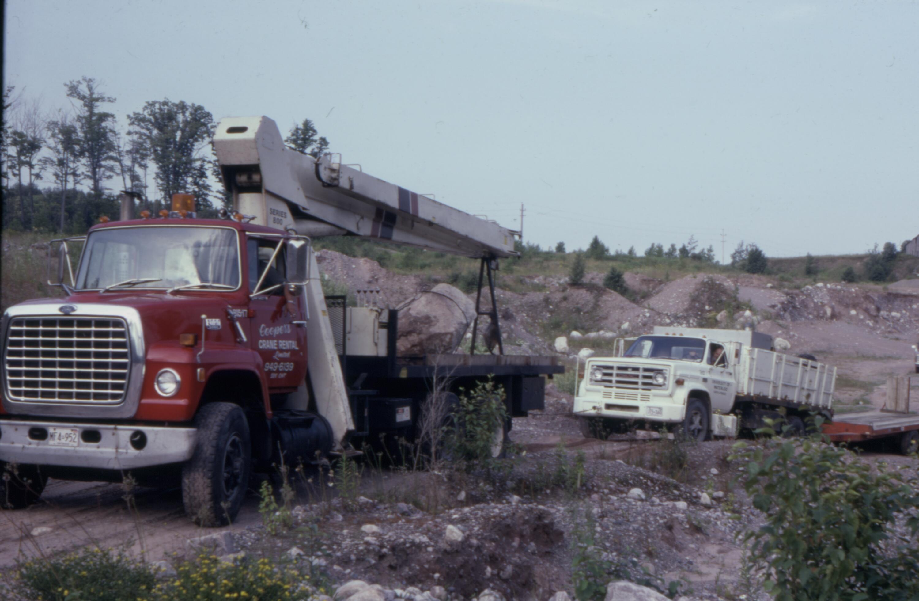 A truck helping another truck get out of the soft sand in a quarry pit.