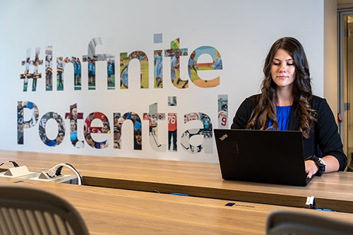 Young professional works at laptop beside backdrop sign that says infinite potential.