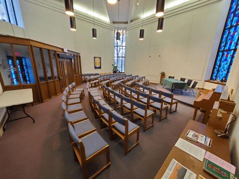 Renison St. Bede Chapel with several rows of chairs set up, with a table and chairs at the front. 