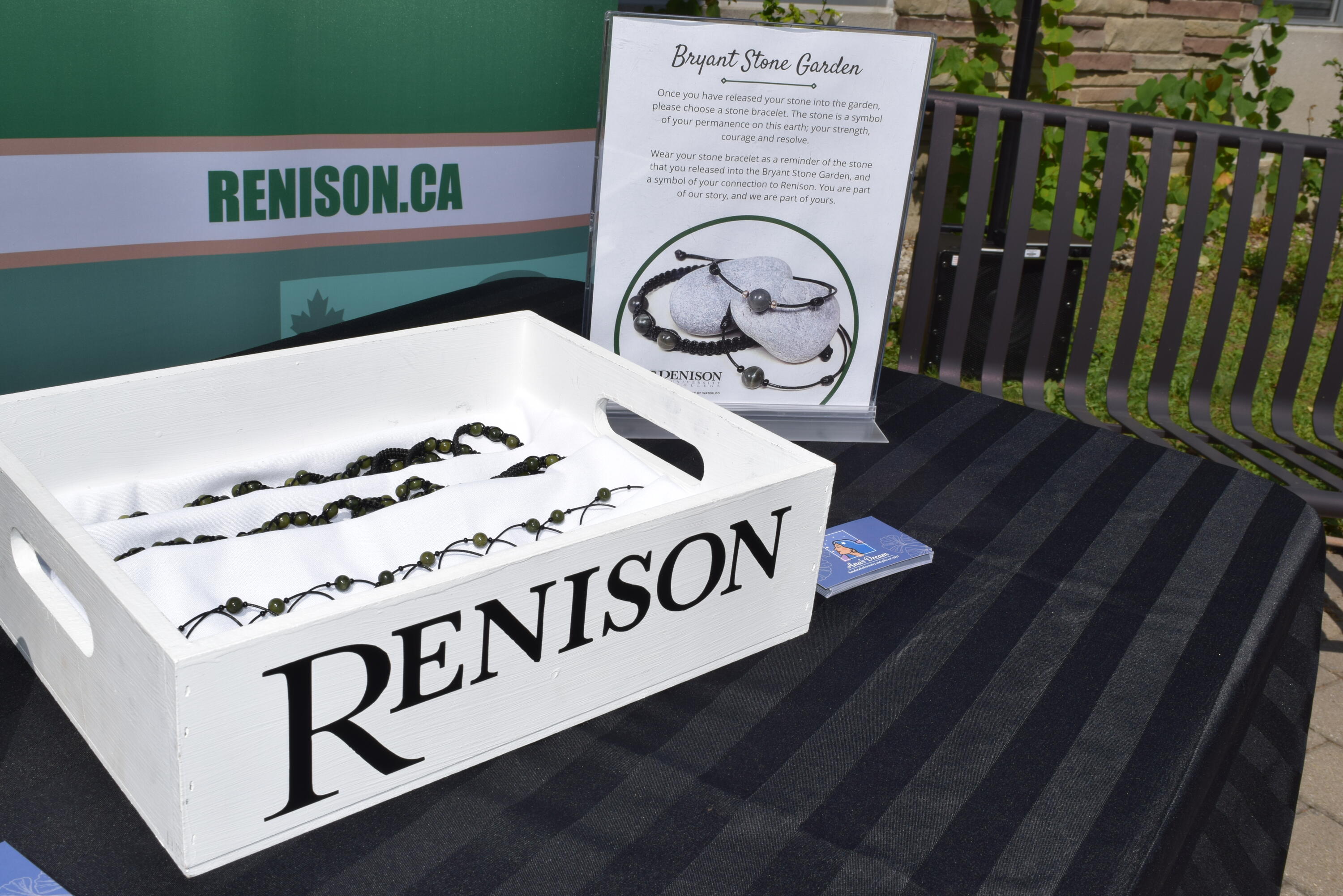 A box with the Renison logo is shown, filled with bracelets that are made of cord with a stone in the centre.