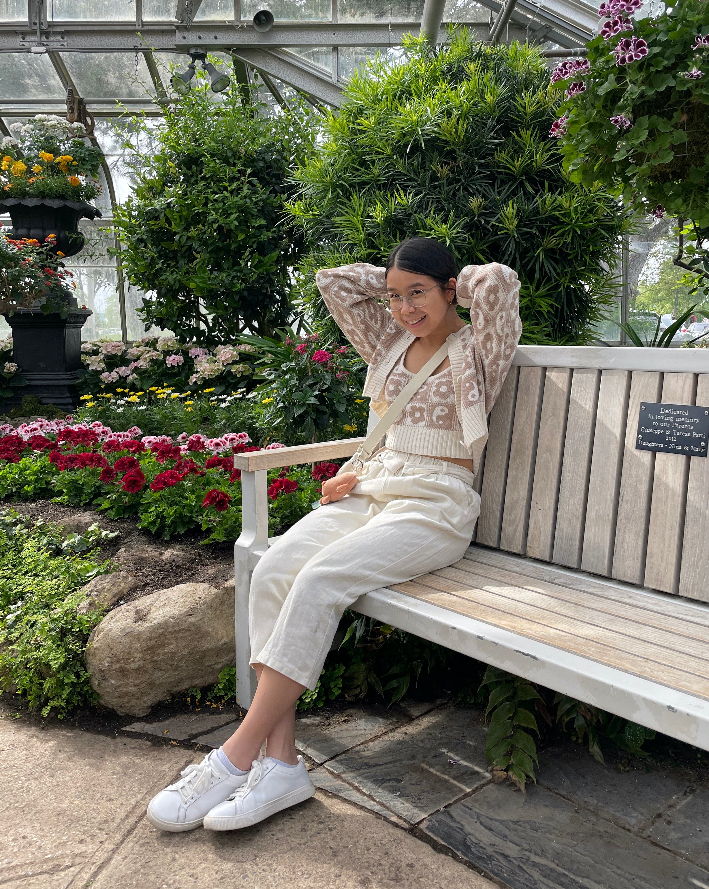 Full body shot of Emily sitting on a bench in a greenhouse