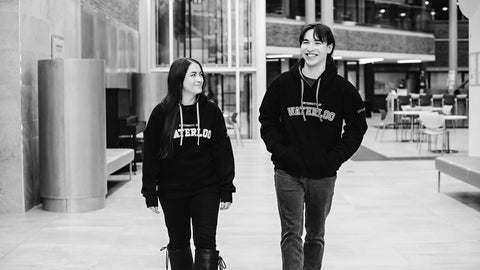 Two indigenous students walking on campus, both wearing Waterloo sweatshirts.