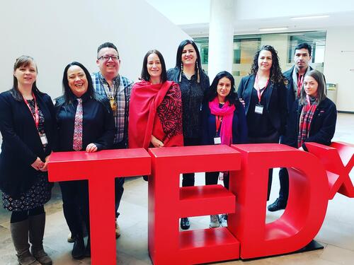 staff and students gather behind the red TEDx sign