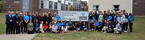 staff, faculty and students sitting and standing around the united college sign.