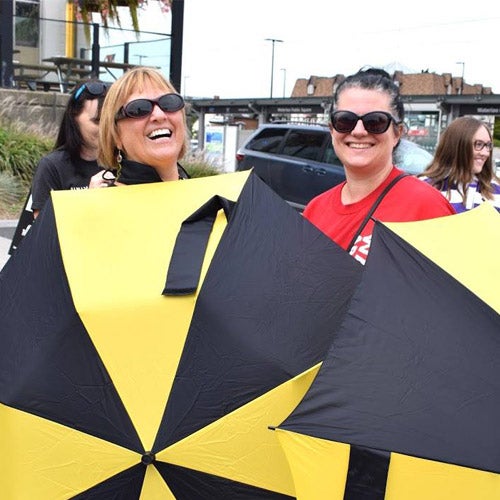 Two staff members holding their gold and black umbrellas