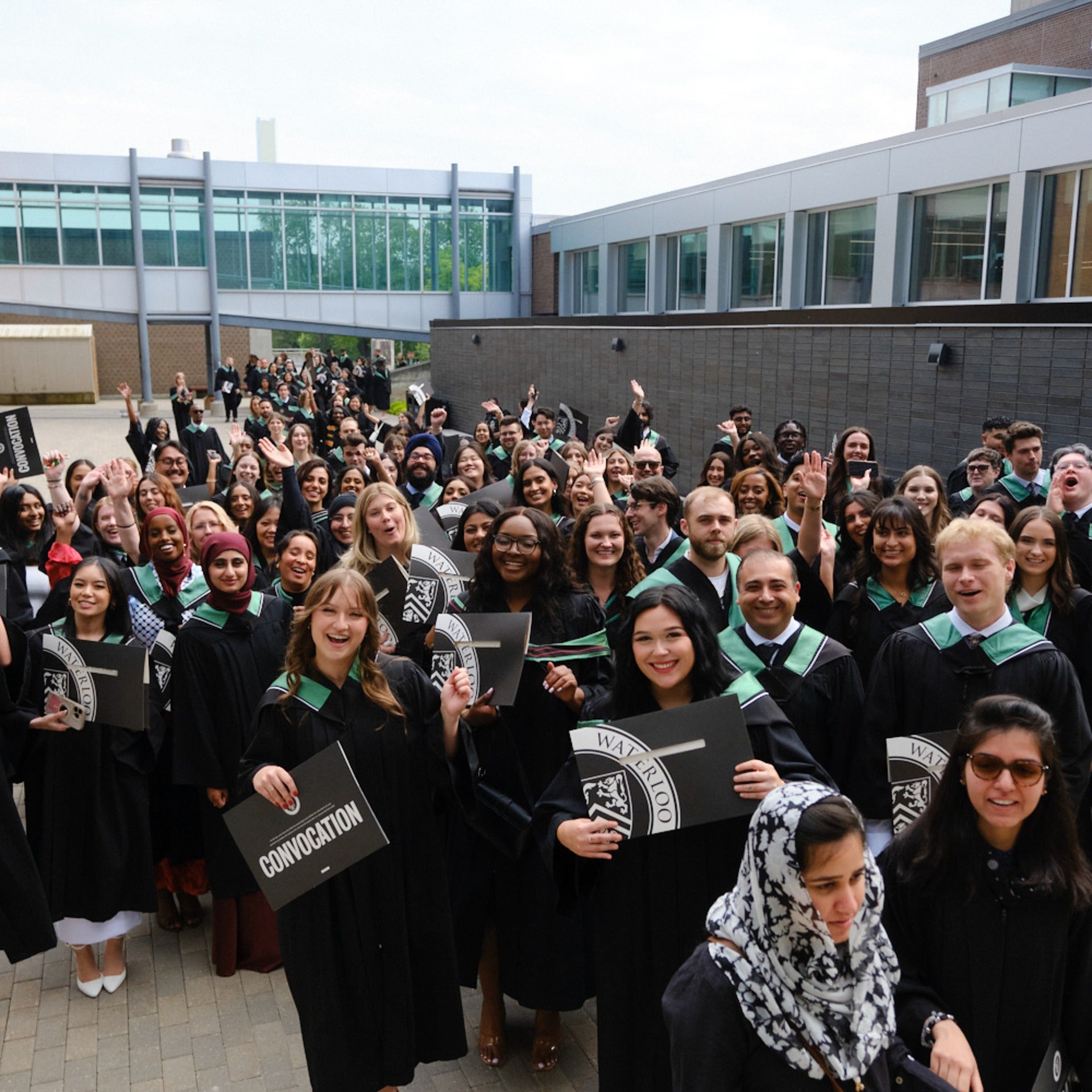 Class of 2025 graduates from the Faculty of Arts holding their diplomas out front of the Physical Activities Complex building