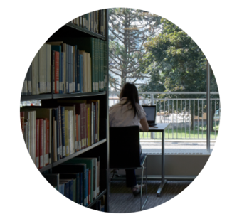 girl studying on her laptop in a library next to bookshelves