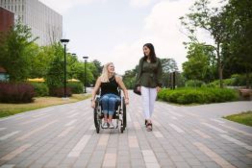 A woman walking beside another woman in a wheelchair.