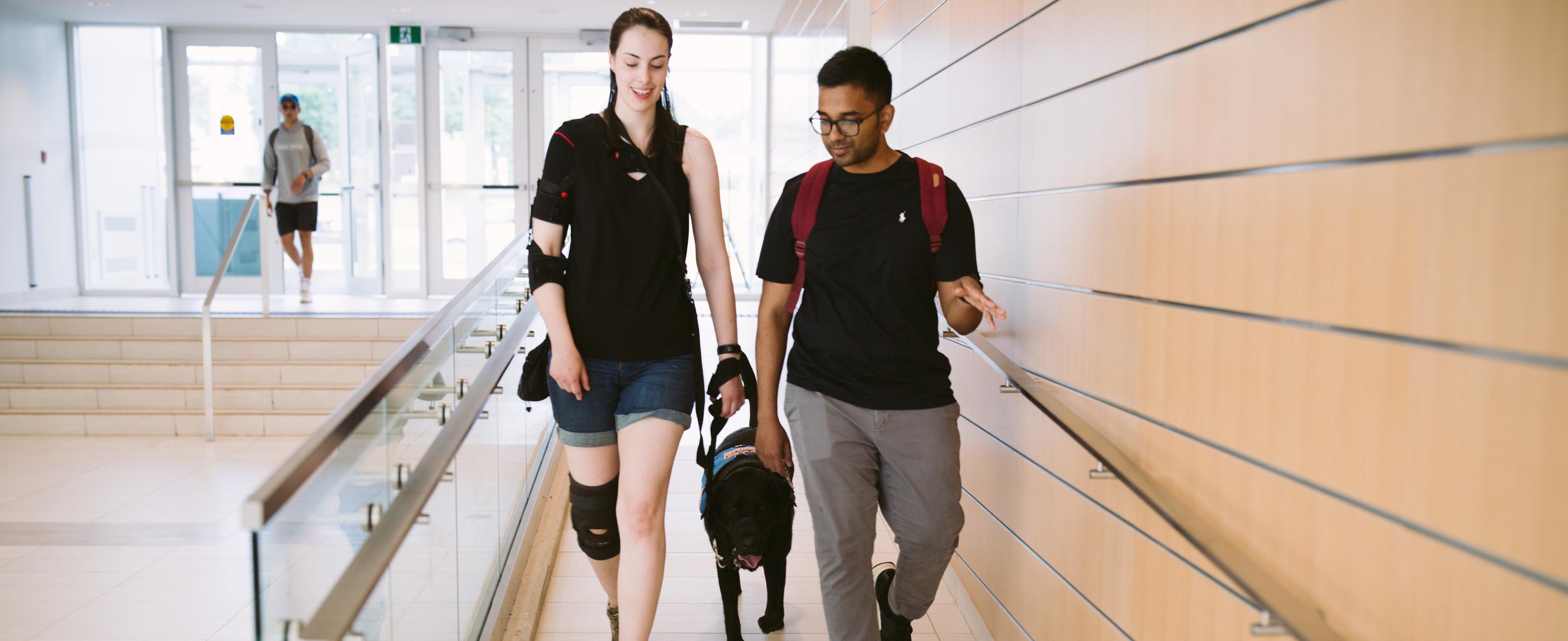 A woman and a man walking down a ramp with a black service dog.