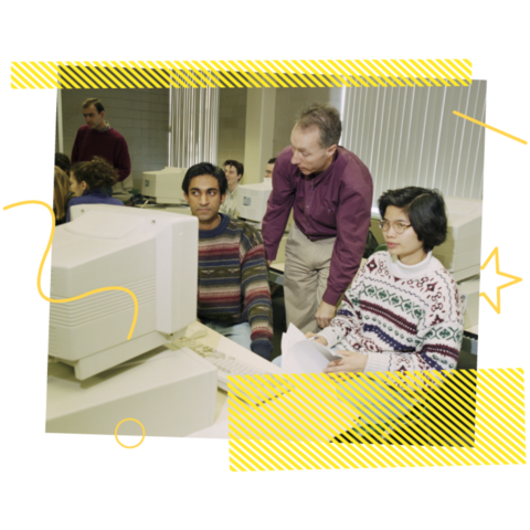 Professor talking to two students near a computer in a lab