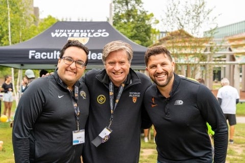 Three alumni pose in Waterloo gear on campus